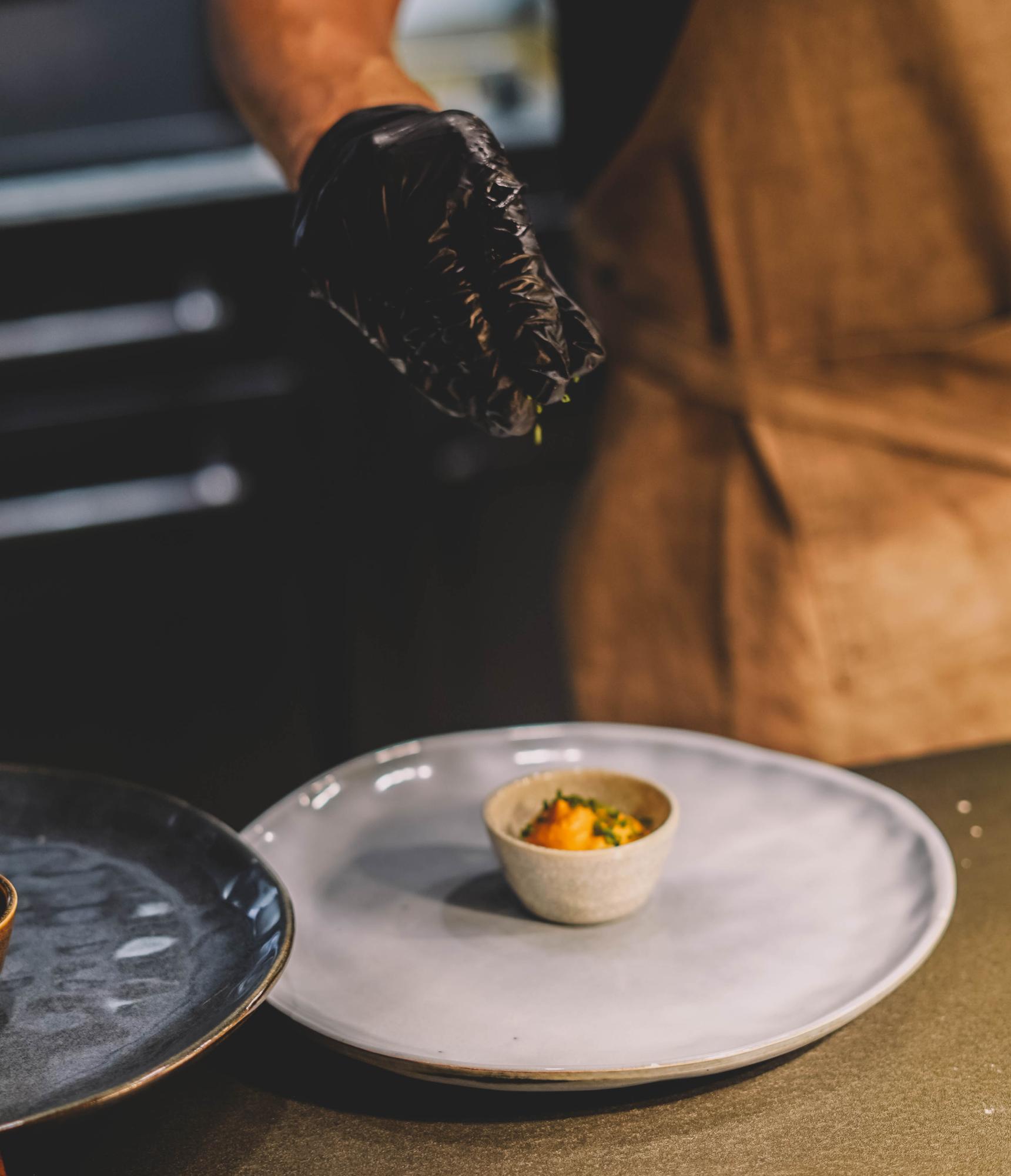 Chef arranging a plated dish on a dark table